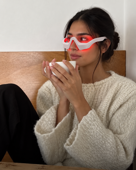 Cliente seduta sul letto con una tazza di caffè e LumiEyes acceso